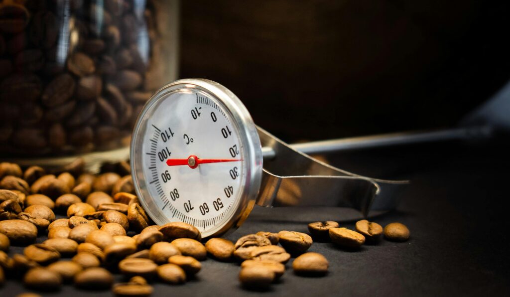 Coffee beans and a thermometer emphasize temperature precision in coffee making.