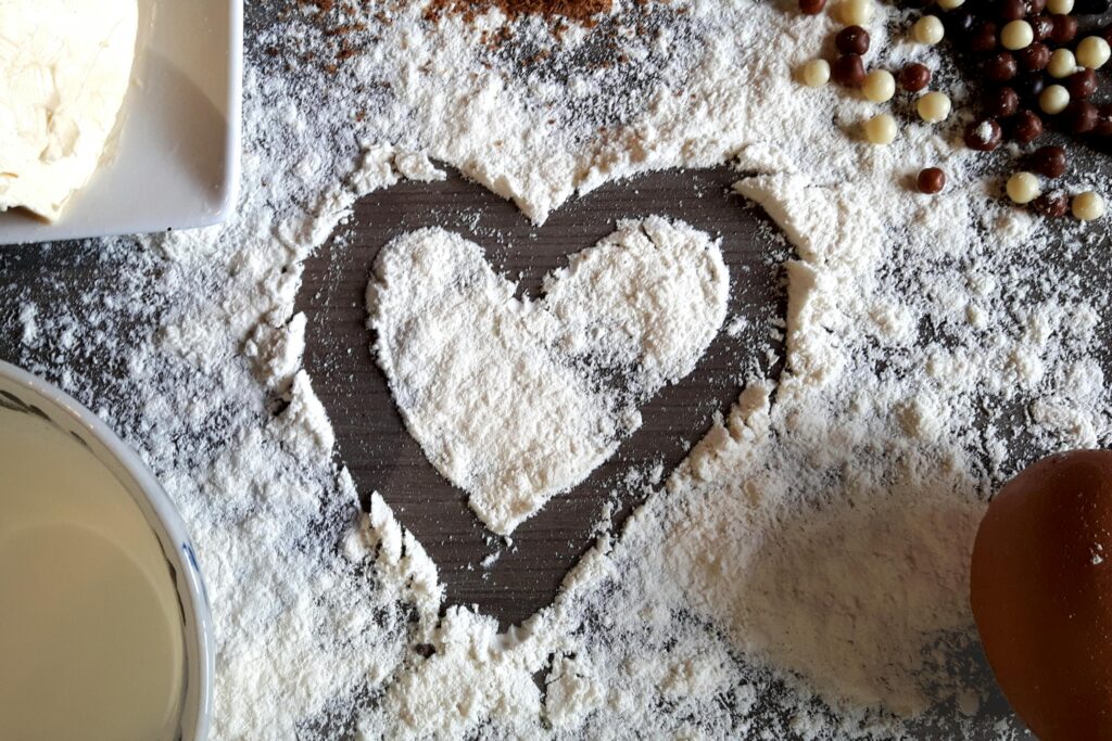 Close-up of a heart shape created in flour, surrounded by baking ingredients.