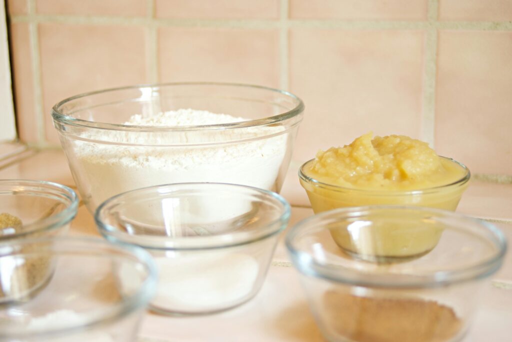 Close-up of glass bowls with flour, applesauce, and sugar, ready for baking.